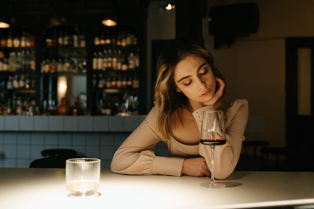 Woman drinks glass of wine alone thinking about her husband